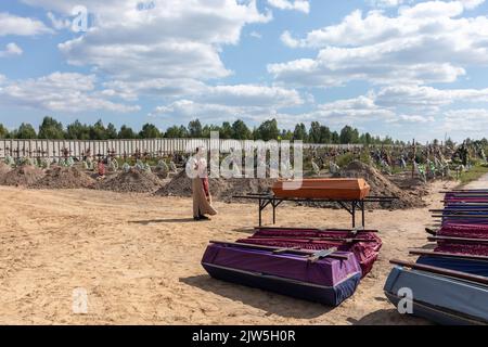 Un prêtre lit une prière et exécute une cérémonie funéraire pour les victimes innocentes de l'agression russe au cimetière de Bucha. Des rangées de cercueils avec des croix et le nombre de victimes non identifiées sont illustrés. Coffins contenant les corps de personnes non identifiées tuées dans le district de Bucha au moment de l'occupation russe, lors d'une cérémonie d'enterrement dans un cimetière de Bucha, région de Kiev, Ukraine. Des mois après le retrait des forces russes du district de Bucha, les corps qui n'ont pas été identifiés ont été enterrés et marqués de numéros dans un cimetière de Bucha. Banque D'Images