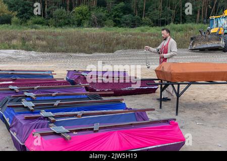 Un prêtre lit une prière et exécute une cérémonie funéraire pour les victimes innocentes de l'agression russe au cimetière de Bucha. Des rangées de cercueils avec des croix et le nombre de victimes non identifiées sont illustrés. Coffins contenant les corps de personnes non identifiées tuées dans le district de Bucha au moment de l'occupation russe, lors d'une cérémonie d'enterrement dans un cimetière de Bucha, région de Kiev, Ukraine. Des mois après le retrait des forces russes du district de Bucha, les corps qui n'ont pas été identifiés ont été enterrés et marqués de numéros dans un cimetière de Bucha. Banque D'Images