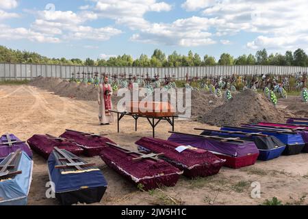 Un prêtre lit une prière et exécute une cérémonie funéraire pour les victimes innocentes de l'agression russe au cimetière de Bucha. Des rangées de cercueils avec des croix et le nombre de victimes non identifiées sont illustrés. Coffins contenant les corps de personnes non identifiées tuées dans le district de Bucha au moment de l'occupation russe, lors d'une cérémonie d'enterrement dans un cimetière de Bucha, région de Kiev, Ukraine. Des mois après le retrait des forces russes du district de Bucha, les corps qui n'ont pas été identifiés ont été enterrés et marqués de numéros dans un cimetière de Bucha. Banque D'Images