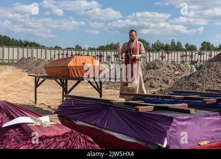 Un prêtre lit une prière et exécute une cérémonie funéraire pour les victimes innocentes de l'agression russe au cimetière de Bucha. Des rangées de cercueils avec des croix et le nombre de victimes non identifiées sont illustrés. Coffins contenant les corps de personnes non identifiées tuées dans le district de Bucha au moment de l'occupation russe, lors d'une cérémonie d'enterrement dans un cimetière de Bucha, dans la région de Kiev, en Ukraine. Des mois après le retrait des forces russes du district de Bucha, les corps qui n'ont pas été identifiés ont été enterrés et marqués de numéros dans un cimetière de Bucha. (Photo de Mykhaylo Palin Banque D'Images