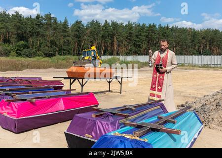 Un prêtre lit une prière et exécute une cérémonie funéraire pour les victimes innocentes de l'agression russe au cimetière de Bucha. Des rangées de cercueils avec des croix et le nombre de victimes non identifiées sont illustrés. Coffins contenant les corps de personnes non identifiées tuées dans le district de Bucha au moment de l'occupation russe, lors d'une cérémonie d'enterrement dans un cimetière de Bucha, dans la région de Kiev, en Ukraine. Des mois après le retrait des forces russes du district de Bucha, les corps qui n'ont pas été identifiés ont été enterrés et marqués de numéros dans un cimetière de Bucha. (Photo de Mykhaylo Palin Banque D'Images