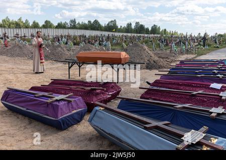 Bucha, Ukraine. 2nd septembre 2022. Un prêtre lit une prière et exécute une cérémonie funéraire pour les victimes innocentes de l'agression russe au cimetière de Bucha. Des rangées de cercueils avec des croix et le nombre de victimes non identifiées sont illustrés. Coffins contenant les corps de personnes non identifiées tuées dans le district de Bucha au moment de l'occupation russe, lors d'une cérémonie d'enterrement dans un cimetière de Bucha, dans la région de Kiev, en Ukraine. Des mois après le retrait des forces russes du district de Bucha, les corps qui n'ont pas été identifiés ont été enterrés et marqués de numéros dans un cimetière Banque D'Images