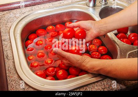 Les mains d'une femme laver les tomates sous l'eau courante dans l'évier de cuisine. Banque D'Images