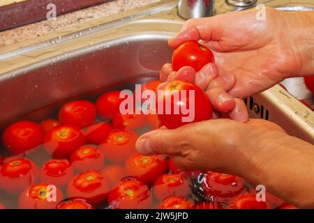Les mains d'une femme laver les tomates sous l'eau courante dans l'évier de cuisine. Banque D'Images