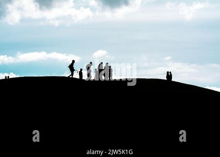 Les silhouettes d'un groupe de personnes marchant sur une colline sous un ciel nuageux Banque D'Images