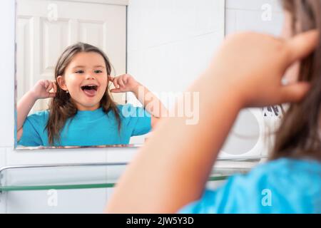 Enfant fille teasing réflexion dans le miroir de salle de bains Banque D'Images