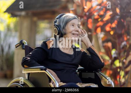Femme asiatique senior écoutant de la musique avec un casque dans l'arrière-cour. Banque D'Images
