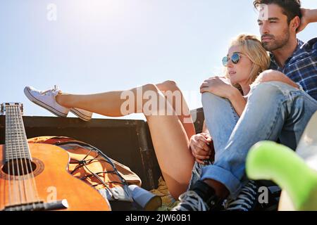 Nous adorons la vue, nous adorons la route. Un jeune couple se détend à l'arrière d'un pick-up pendant un voyage en voiture. Banque D'Images