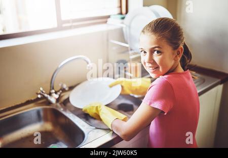 Plus de mains autour de la maison équivaut à moins de travail. Portrait d'une jeune fille gaie laver des plats avec des gants jaunes à la maison tout en regardant le Banque D'Images