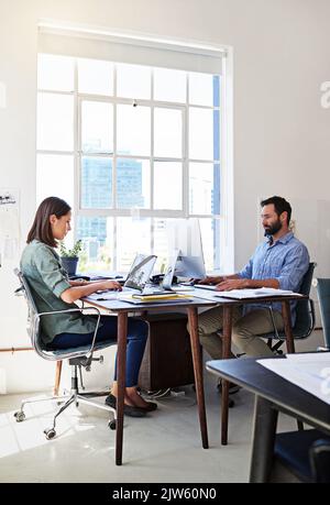 S'engage à faire de leur mieux. Collègues travaillant sur leurs ordinateurs à un bureau dans un bureau ouvert. Banque D'Images