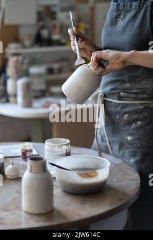 Jeune artisan peint vase avec pinceau après la cuisson et façonnage fait à la main en studio Banque D'Images