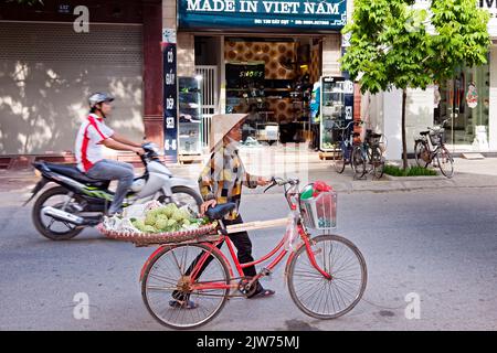 Marchand vietnamien portant chapeau de bambou vendant des légumes sur vélo, Hai Phong, Vietnam Banque D'Images