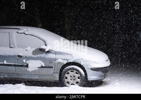 Varsovie, Pologne - 30 janvier 2021 : temps d'hiver avec chute de neige. Une voiture debout sous la lanterne la nuit, couverte de neige. Banque D'Images