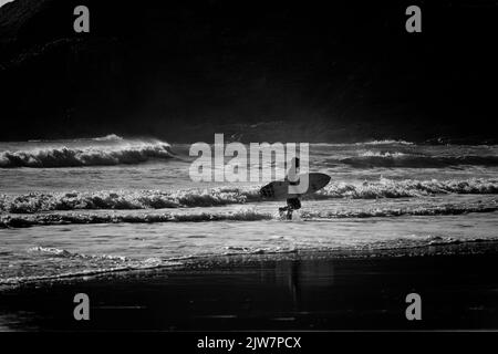 Surfeurs profitant des vagues à la plage de sable de Gwithian Cornwall. Noir et blanc. Banque D'Images