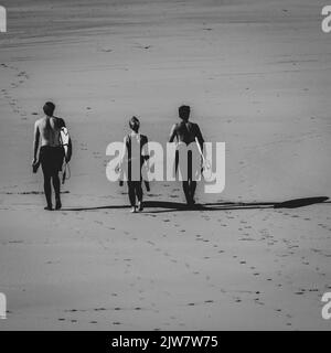 Les hommes et les femmes surfent sur la plage et attrapent les vagues sur la plage de sable de Gwithian. Noir et blanc. Banque D'Images