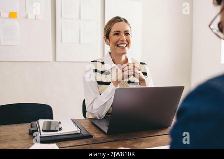 Le gestionnaire d'embauche est enthousiaste à l'idée de sourire en souriant tout en interviewant un candidat à un poste dans son bureau. Bonne femme d'affaires ayant une réunion avec un ap sélectionné Banque D'Images