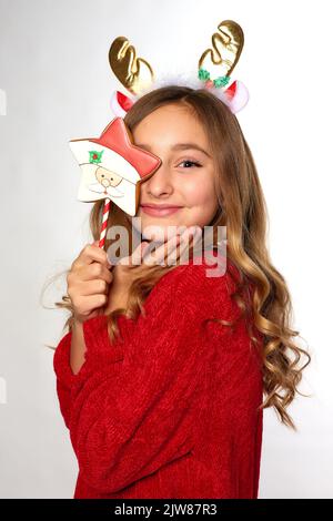 petite fille souriante tient le père noël en pain d'épice sur le bâton dans les mains sur fond blanc Banque D'Images