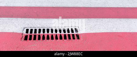 Grilles métalliques pour le drainage des eaux de pluie sur la surface de la route asphaltée sur le passage pour piétons peintes en bandes rouges et blanches Banque D'Images