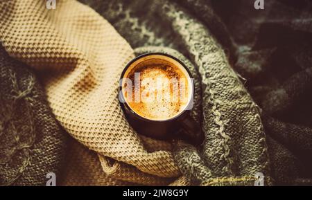 Parmi les pulls chauds en laine, il y a une tasse noire avec du café chaud à la cannelle. Une boisson chaude et revigorante pendant la saison froide. Confort à la maison. HYG Banque D'Images