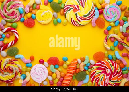 Sucettes colorées et bonbons ronds de différentes couleurs sur jaune Banque D'Images