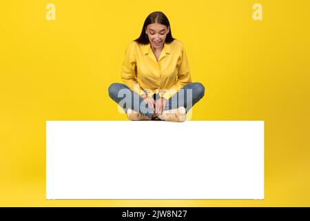 Femme assise sur papier vierge offre de publicité sur tableau, fond jaune Banque D'Images