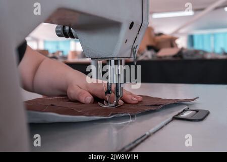 Les coutures de couturière à la machine à coudre filent le tissu. Mains des femmes Banque D'Images