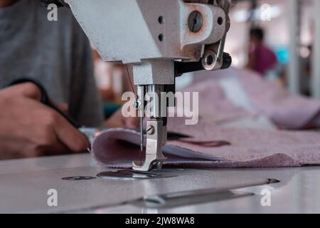 Une couturière coupe le tissu en travaillant à une machine à coudre dans l'atelier. Mains des femmes Banque D'Images