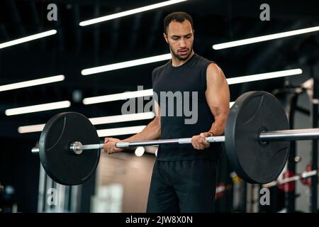 Beau athlète masculin noir s'exerçant avec Heavy Barbell à l'intérieur de salle de gym moderne Banque D'Images