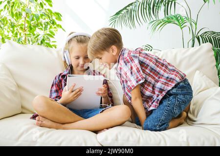 Des enfants adorables avec un casque qui profite de la tablette à la maison. Banque D'Images