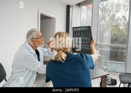 Une équipe de médecins discute des résultats d'une radiographie ou d'une IRM de la colonne vertébrale du patient dans le bureau de médecine de la clinique Banque D'Images