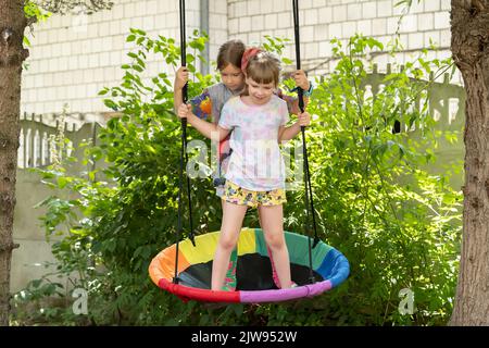 Deux filles, des enfants se tenant ensemble sur une balançoire dans le jardin, s'amuser à l'extérieur, sourire. Activités estivales amusantes, sœurs, frères et sœurs, amis bondin Banque D'Images