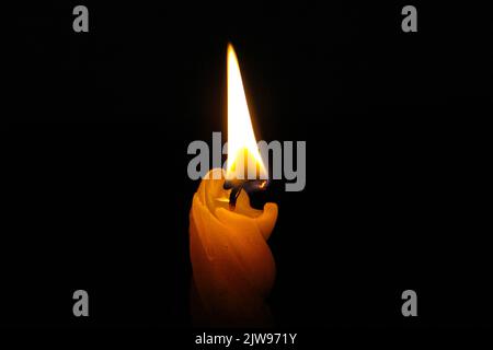 La bougie brûle dans l'obscurité. Une bougie de cire jaune brûle avec une flamme vive dans l'obscurité absolue. Gros plan. Feu la nuit. Religion et prière. Banque D'Images