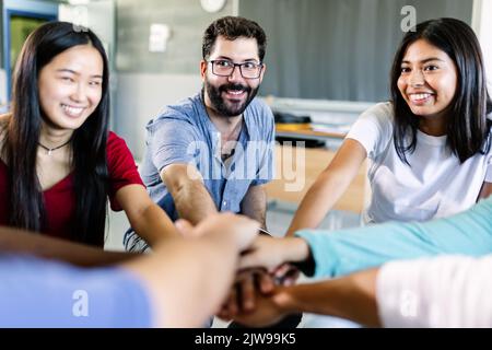 Jeune groupe diversifié d'élèves empilant les mains avec un enseignant de sexe masculin en salle de classe Banque D'Images