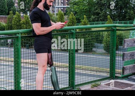 Jeune homme avec une jambe prothétique utilisant les médias sociaux avec son smartphone Banque D'Images