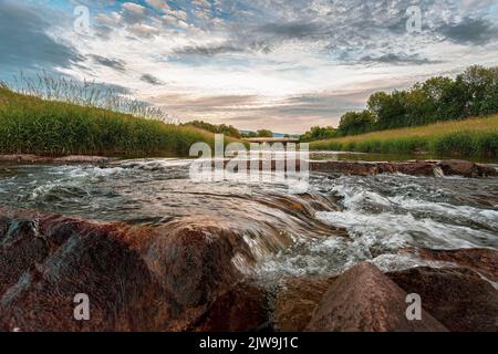 Un beau paysage d'eau qui coule à travers des rochers avec de la verdure autour et ciel nuageux Banque D'Images