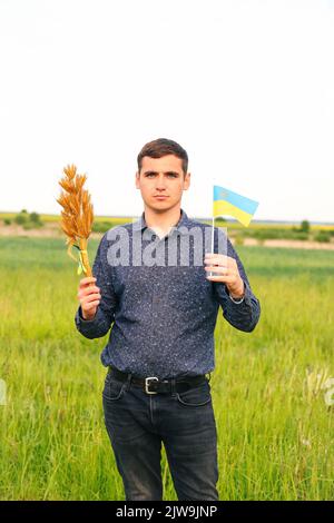 Recentrer le jeune homme portant le drapeau ukrainien et les épis de blé de blé attachés et le drapeau sur le fond de la nature du pré. Drapeau de l'Ukraine. Liberté. Les hommes ukrainiens Banque D'Images