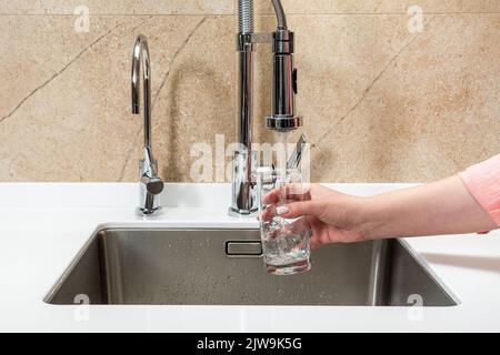 Quelqu'un aspire l'eau du robinet de la cuisine dans un verre Banque D'Images