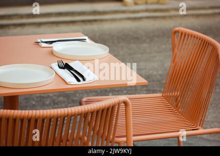 Café-terrasse moderne, restaurant sur un trottoir d'une rue de la ville. Chaises aux couleurs rétro rose pêche, table avec plats servis, assiettes, couverts. PLA élégant Banque D'Images