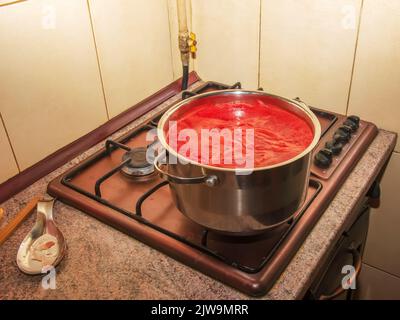 Une femme prépare du jus frais et sain à partir de tomates. Le jus de tomate fraîchement préparé est bouilli dans une casserole et conservé pour un stockage à long terme. Le régime alimentaire concep Banque D'Images