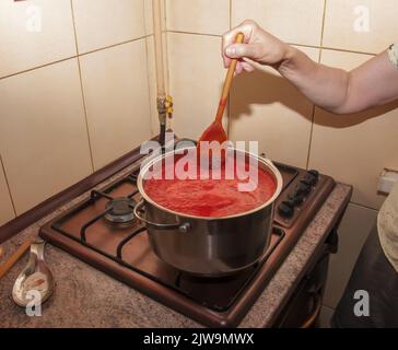 Une femme prépare du jus frais et sain à partir de tomates. Le jus de tomate fraîchement préparé est bouilli dans une casserole et conservé pour un stockage à long terme. Le régime alimentaire concep Banque D'Images