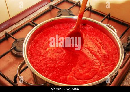 Une femme prépare du jus frais et sain à partir de tomates. Le jus de tomate fraîchement préparé est bouilli dans une casserole et conservé pour un stockage à long terme. Le régime alimentaire concep Banque D'Images