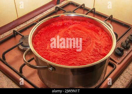 Une femme prépare du jus frais et sain à partir de tomates. Le jus de tomate fraîchement préparé est bouilli dans une casserole et conservé pour un stockage à long terme. Le régime alimentaire concep Banque D'Images