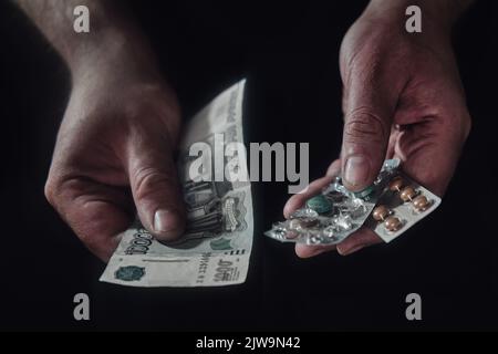 Argent en roubles russes et pilules dans les mains d'un homme sur fond noir Banque D'Images