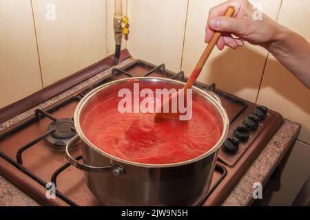 Une femme prépare du jus frais et sain à partir de tomates. Le jus de tomate fraîchement préparé est bouilli dans une casserole et conservé pour un stockage à long terme. Le régime alimentaire concep Banque D'Images