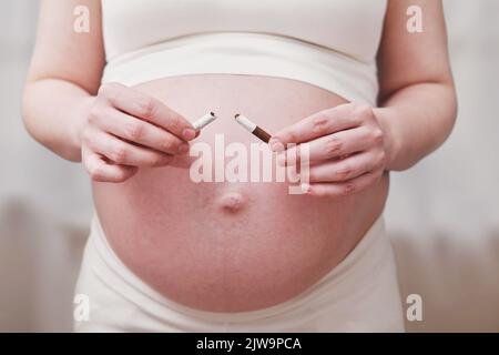 La femme enceinte casse une cigarette dans ses mains comme arrêt du tabagisme, salon à la maison Banque D'Images