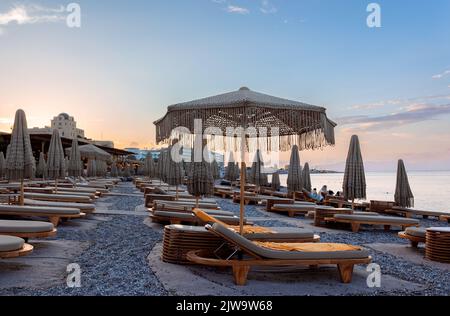 Vue panoramique sur la mer Méditerranée depuis la plage avec parasols fermés et chaises longues sur fond de coucher de soleil coloré de Rhodes, Grèce. Photo de haute qualité Banque D'Images