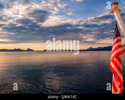 Coucher de soleil et silhouette collines et terre lointaines avec foyer sur le drapeau américain de premier plan sur la poupe de bateau dans l'image de voyage de l'Alaska. Banque D'Images