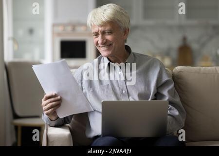 Joyeux homme mûr aux cheveux gris travaillant à la maison Banque D'Images