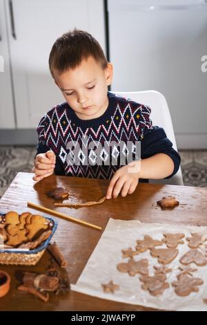 Un garçon prépare des biscuits au pain d'épice dans la cuisine. Traditions familiales de Noël. Loisirs de l'enfant pendant les vacances du nouvel an. Banque D'Images