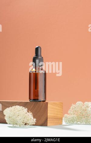 Flacon avec pipette en verre foncé, produit cosmétique woodenpiédestal. Fond de corail pastel Banque D'Images